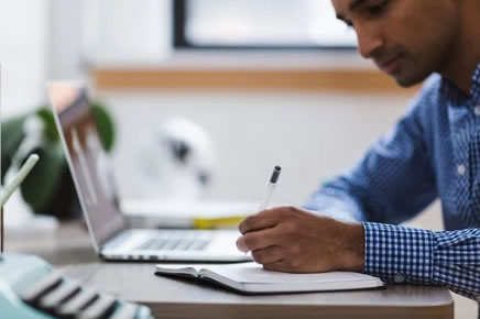 Man Working at Computer Taking Notes